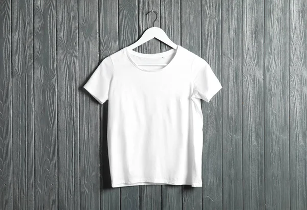 Kleiderbügel mit weißem T-Shirt auf Holzgrund. Design-Attrappe — Stockfoto