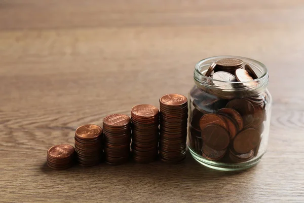 Pot en verre et piles de pièces de monnaie sur table en bois. Concept d'économie — Photo