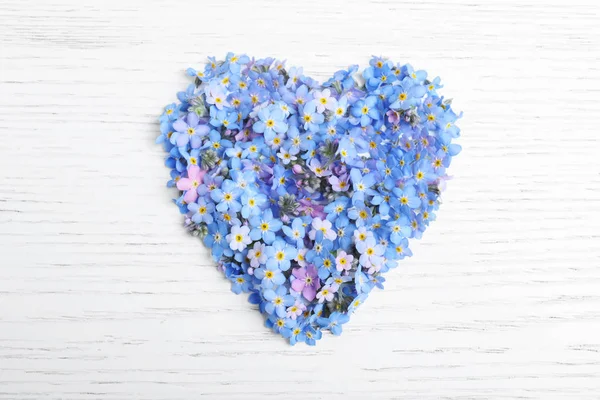 Heart made of forget-me-not flowers on white wooden background, top view