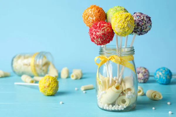 Yummy bright cake pops in glass jar full of sweets on table. Space for text