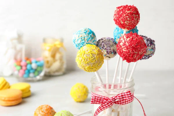 Yummy bright cake pops in glass jar full of marshmallows on table. Space for text
