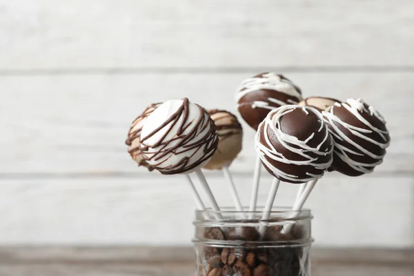 Leckere Cake Pops mit Schokolade im Glas voller Kaffeebohnen auf verschwommenem Hintergrund, Nahaufnahme. Raum für Text — Stockfoto