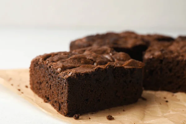 Pergamentpapier mit frischen Brownies auf weißem Tisch, Platz für Text. leckerer Schokoladenkuchen — Stockfoto