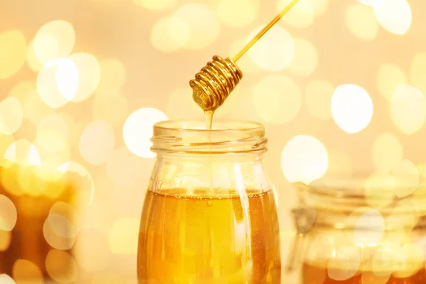 Μέλι στάζει από κουτάλα σε βάζο εναντίον θολή φώτα, κοντινό πλάνο — Φωτογραφία Αρχείου