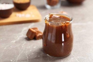 Gri masada lezzetli karamel soslu kavanoz. Metin için alan