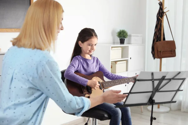 Маленька дівчинка грає на гітарі зі своїм вчителем на уроці музики. Навчальні нотатки — стокове фото