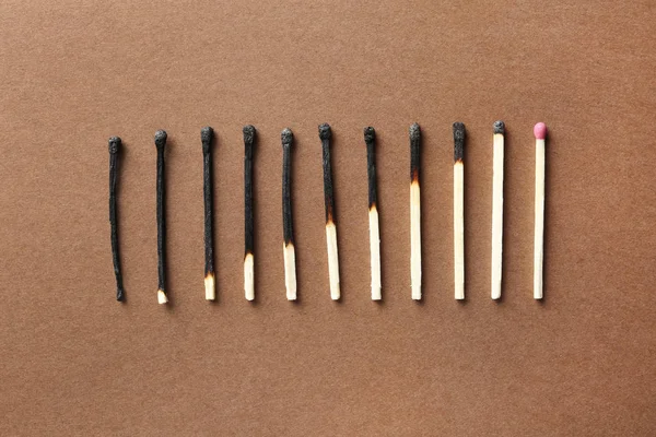 Row of burnt matches and whole one on color background, flat lay. Human life phases concept — Stock Photo, Image