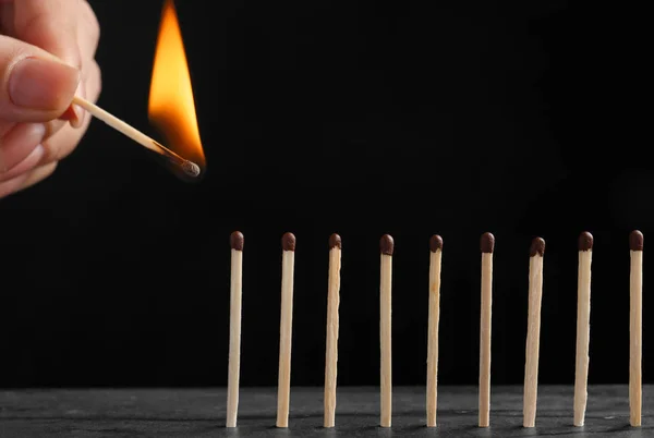 stock image Woman igniting line of matches on table against dark background, closeup. Space for text