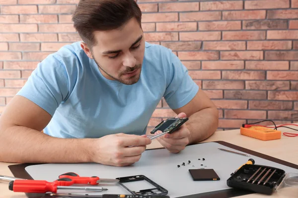 Техник по ремонту сломанного смартфона за столом в мастерской — стоковое фото