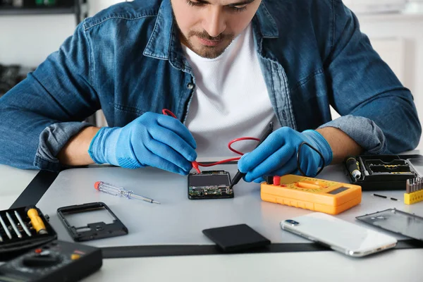 Technicien vérifiant smartphone cassé à la table dans l'atelier de réparation, gros plan — Photo