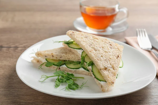 Plate with tasty cucumber sandwiches served on wooden table