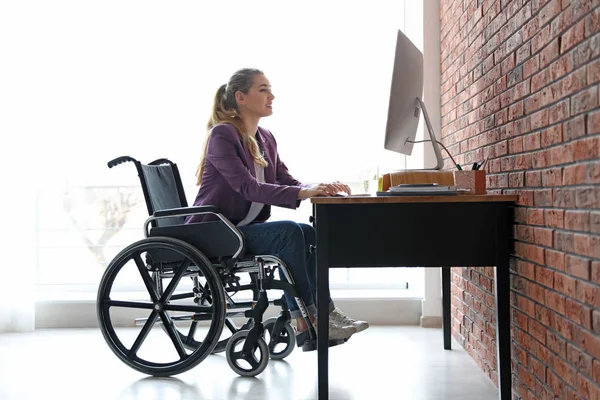 Vrouw in rolstoel werkend met computer aan tafel binnen — Stockfoto