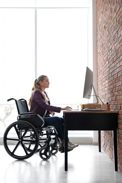 Woman in wheelchair working with computer at table indoors