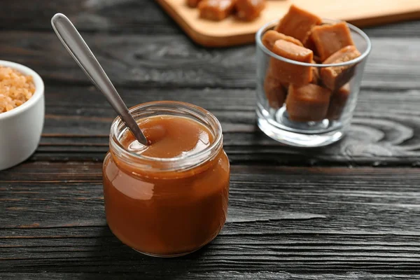 Pot avec sauce caramel savoureuse et cuillère sur table en bois. Espace pour le texte — Photo