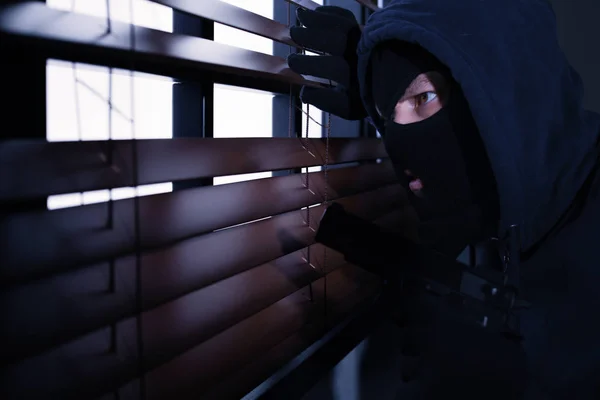 Álarcos ember a fegyvert kémkedett ablakon redőnyök beltéri. Bűncselekmény — Stock Fotó