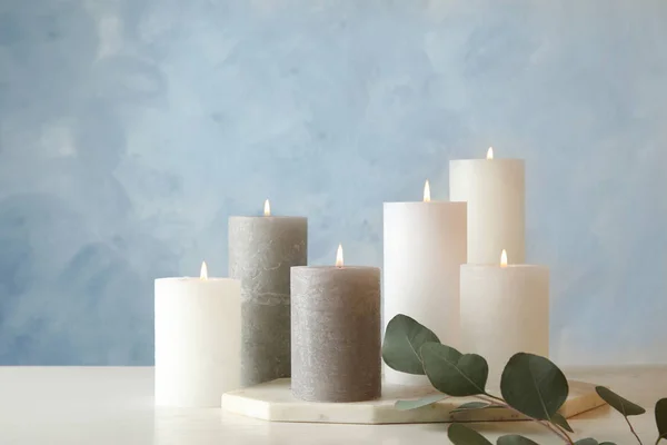 Složení s hořící svíčkami na stole proti barevnému pozadí — Stock fotografie