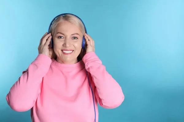 Mujer madura disfrutando de la música en los auriculares en el fondo de color. Espacio para texto —  Fotos de Stock