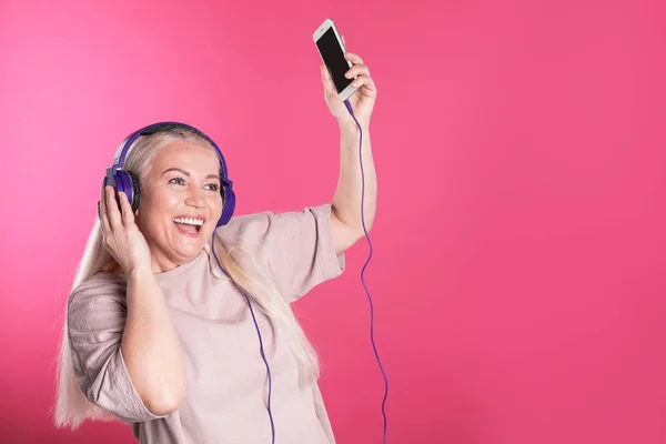Reife Frau mit Kopfhörer und Mobilgerät auf farbigem Hintergrund. Raum für Text — Stockfoto