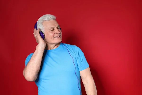 Hombre maduro disfrutando de la música en auriculares sobre fondo de color. Espacio para texto —  Fotos de Stock