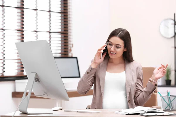 Mujer embarazada joven hablando por teléfono mientras trabaja en la oficina —  Fotos de Stock