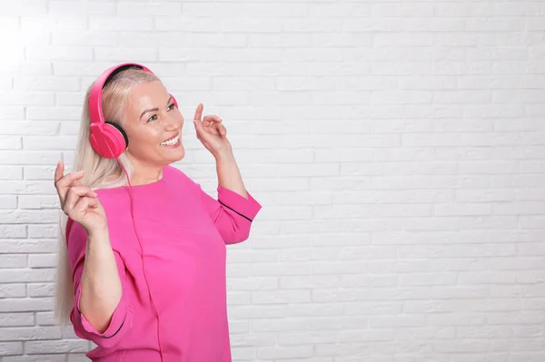 Mature woman enjoying music in headphones against brick wall. Space for text — Stock Photo, Image