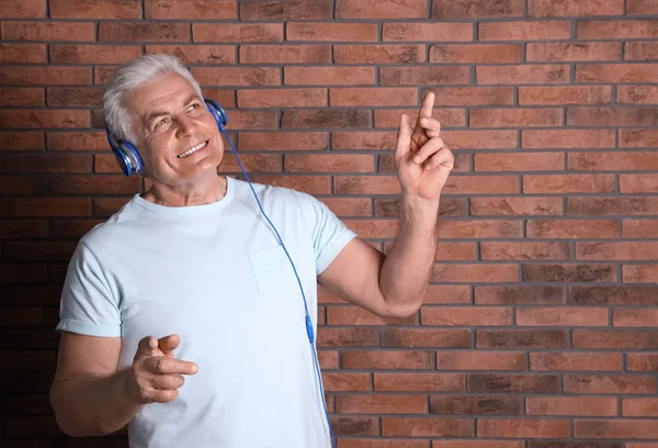 Зрелый мужчина наслаждается музыкой в наушниках против кирпичной стены. Пространство для текста — стоковое фото