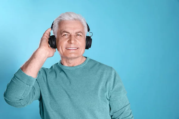 Hombre maduro disfrutando de la música en auriculares sobre fondo de color. Espacio para texto —  Fotos de Stock