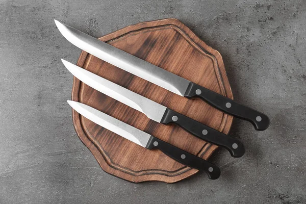 Deska do krojenia i różne noże na szarym tle, płaskie lay — Zdjęcie stockowe