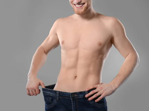 Young man with slim body in old big size jeans on grey background, closeup — Stock Photo, Image