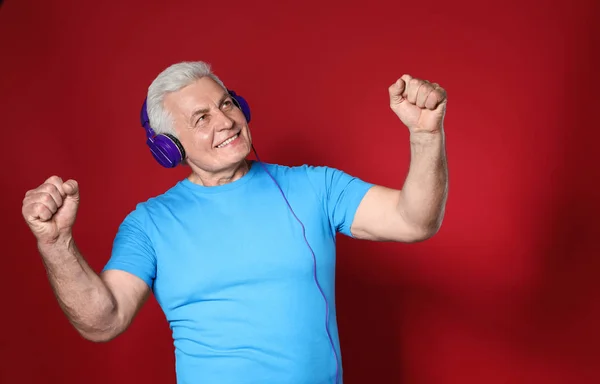 Hombre maduro disfrutando de la música en auriculares sobre fondo de color —  Fotos de Stock