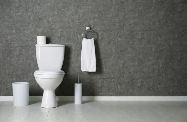 Interior do banheiro simples com vaso sanitário novo perto da parede cinza. Espaço para texto — Fotografia de Stock