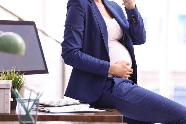 Young pregnant woman in suit at workplace, closeup