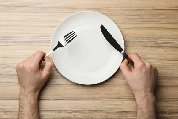 Férfi üres tányéron és evőeszközzel, fa asztallal, felülnézetben — Stock Fotó