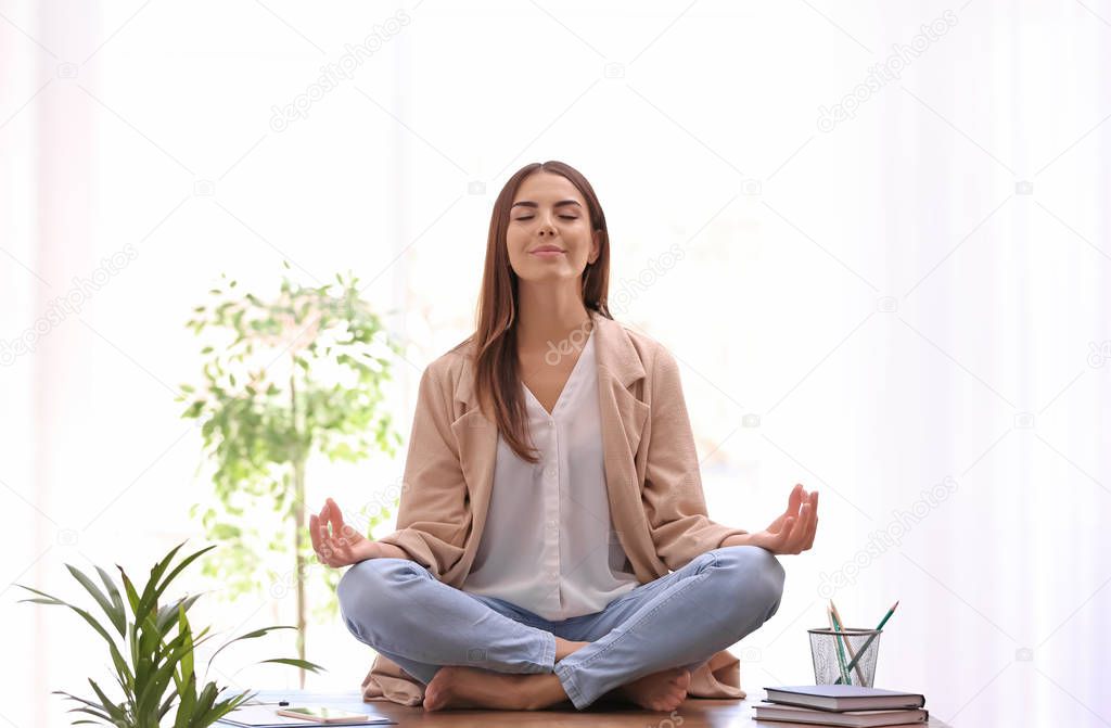 Young businesswoman meditating at workplace. Zen concept