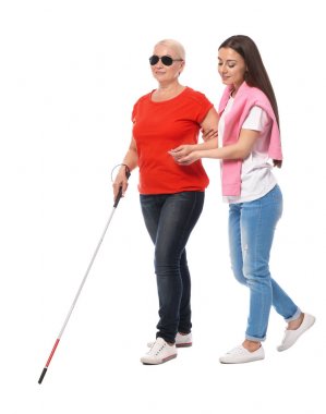 Young woman helping blind person with long cane on white background