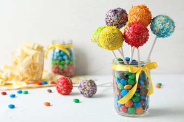 Yummy bright cake pops in glass jar full of candies on table. Space for text