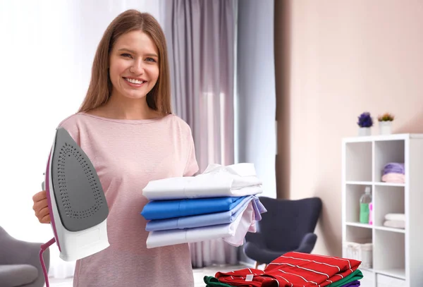 Junge Frau mit zusammengefalteter Kleidung und Bügeleisen zu Hause. Raum für Text — Stockfoto