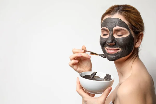 Beautiful woman applying black mask onto face against light background. Space for text — Stock Photo, Image