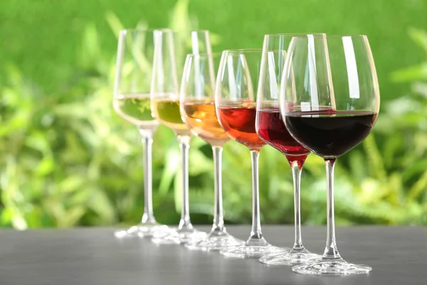 Row of glasses with different wines on grey table against blurred background. Space for text — Stock Photo, Image