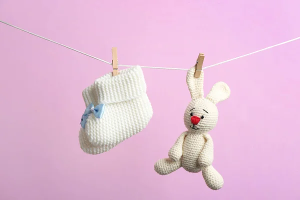 Sapatilhas de malha e coelho de brinquedo pendurado na linha de lavagem contra fundo de cor. Acessórios para bebés — Fotografia de Stock