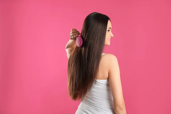 Schöne junge Frau mit Haarbürste auf Farbhintergrund — Stockfoto