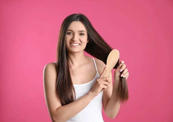 Hermosa joven sonriente con cepillo de pelo sobre fondo de color — Foto de Stock