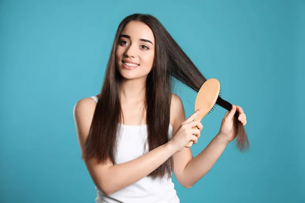 Hermosa joven sonriente con cepillo de pelo sobre fondo de color — Foto de Stock