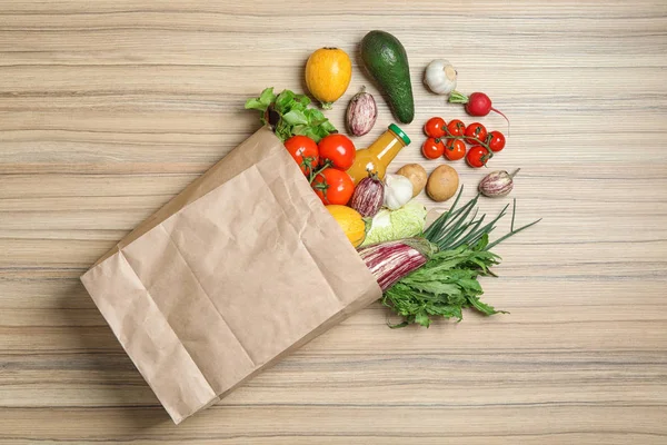 Sac en papier renversé avec légumes, herbes et bouteille de jus sur fond en bois, plat — Photo