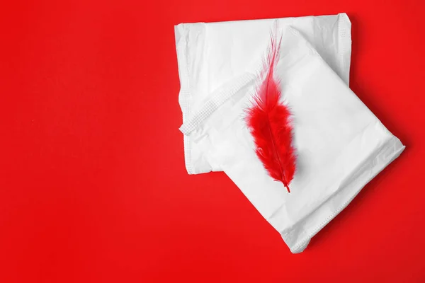 Embalado almofadas menstruais e penas vermelhas no fundo de cor, flat lay com espaço para texto. Cuidados ginecológicos — Fotografia de Stock