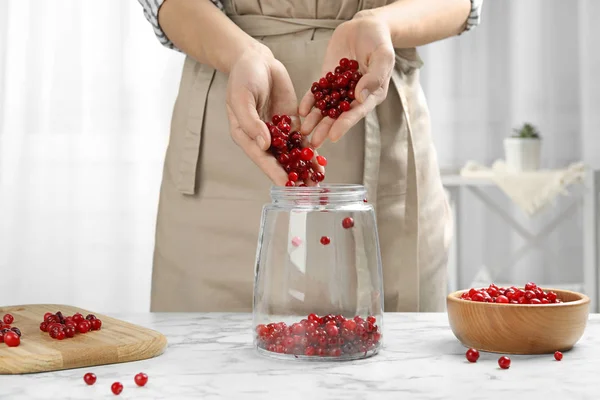 Mulher derramando bagas vermelhas em frasco de vidro na mesa na cozinha, close-up — Fotografia de Stock