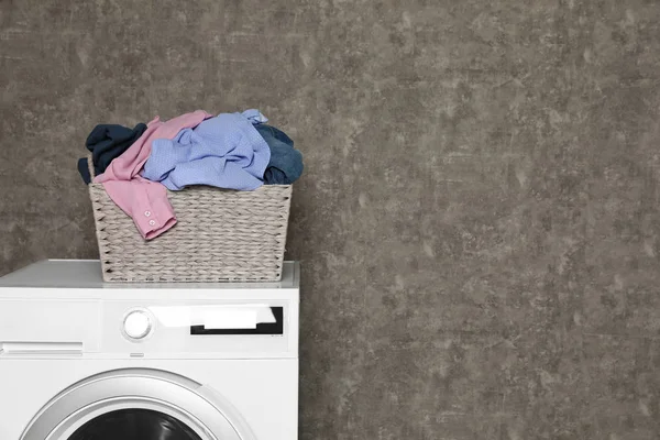 Wicker laundry basket full of dirty clothes on washing machine near color wall. Space for text