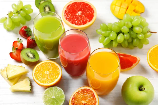 Vasos con diferentes jugos y frutas frescas sobre mesa de madera —  Fotos de Stock