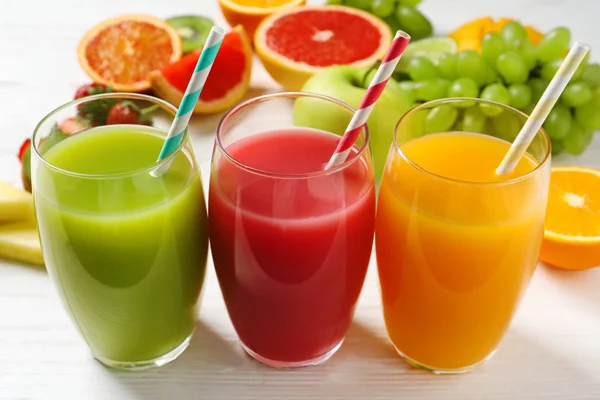 Vasos de diferentes jugos con pajitas y frutas frescas sobre mesa de madera — Foto de Stock