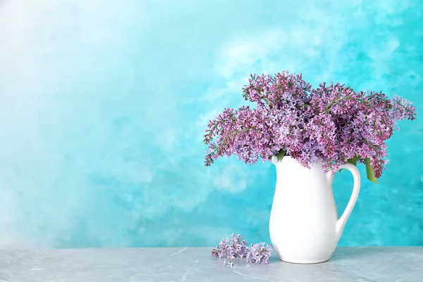 色の背景に対してテーブルの上に磁器ピッチャーでライラックの花を開花。テキスト用のスペース — ストック写真